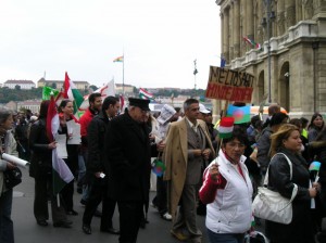 The cardboard sign says 'everyone deserves respect' and the blue-and-green flag with the sunburst is a Roma flag.